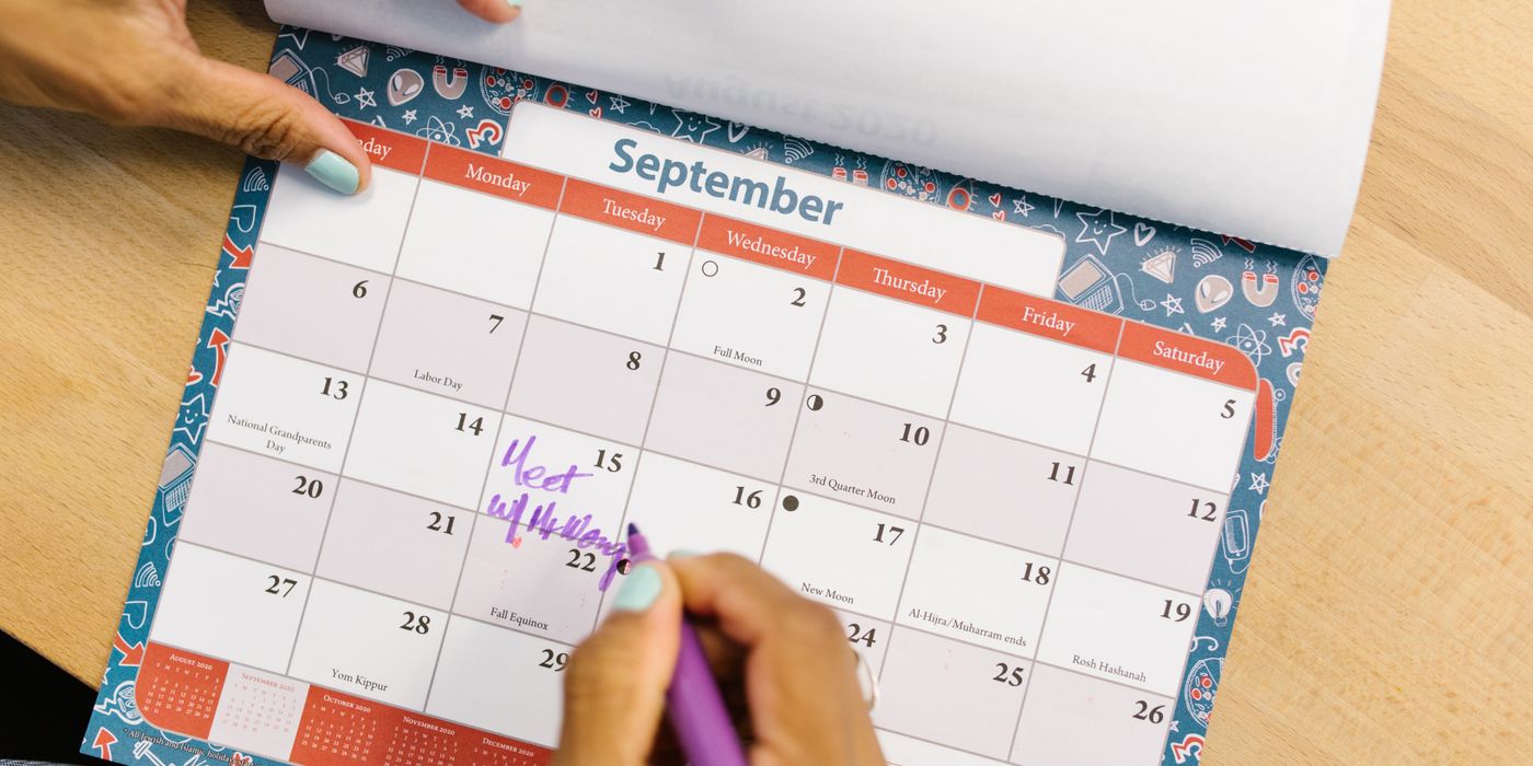 Person marking dates on a September wall calendar while planning a trip