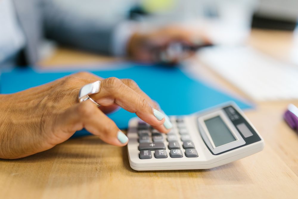 Hand using a desktop calculator on a timber desk beside a blue folder