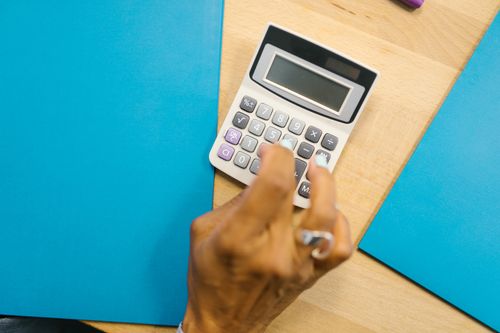 Free A hand using a calculator on a wooden desk surrounded by blue folders. Stock Photo