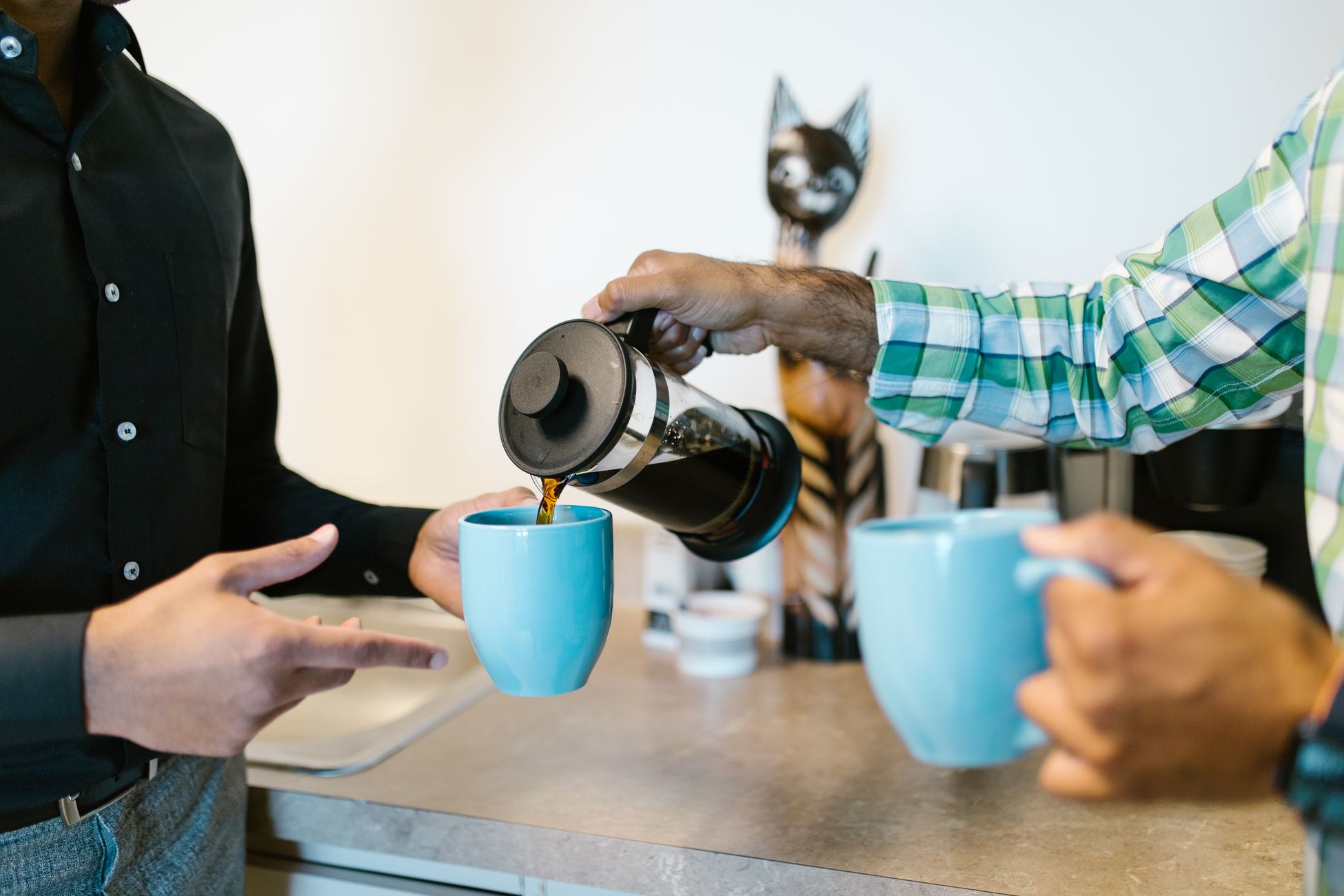 Two coworkers pour fresh coffee into blue mugs during an office coffee break.