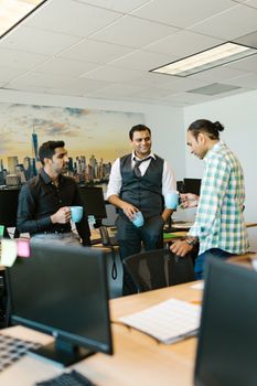 Three colleagues enjoy a casual coffee break in a modern office environment.