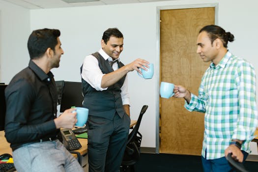 Three colleagues enjoying a coffee break, sharing smiles and conversations in a modern office setting.