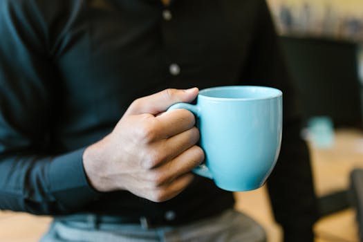 Man's hand holding a blue coffee mug in a professional office setting.