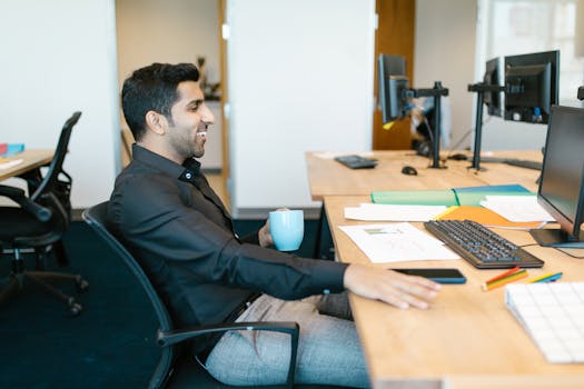 A businessman enjoying a coffee break and smiling while sitting at his desk in a modern office.