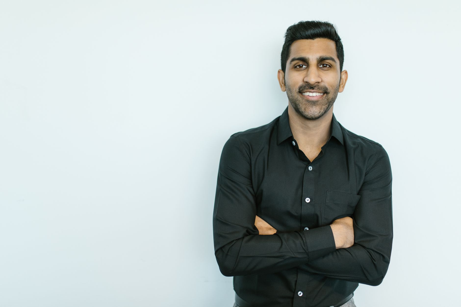 Portrait of a confident man in black shirt smiling against a plain background.