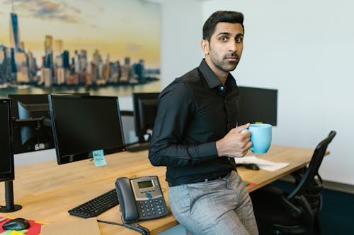 Man in Black Dress Shirt Leaning on a Table Holding Blue Ceramic Mug