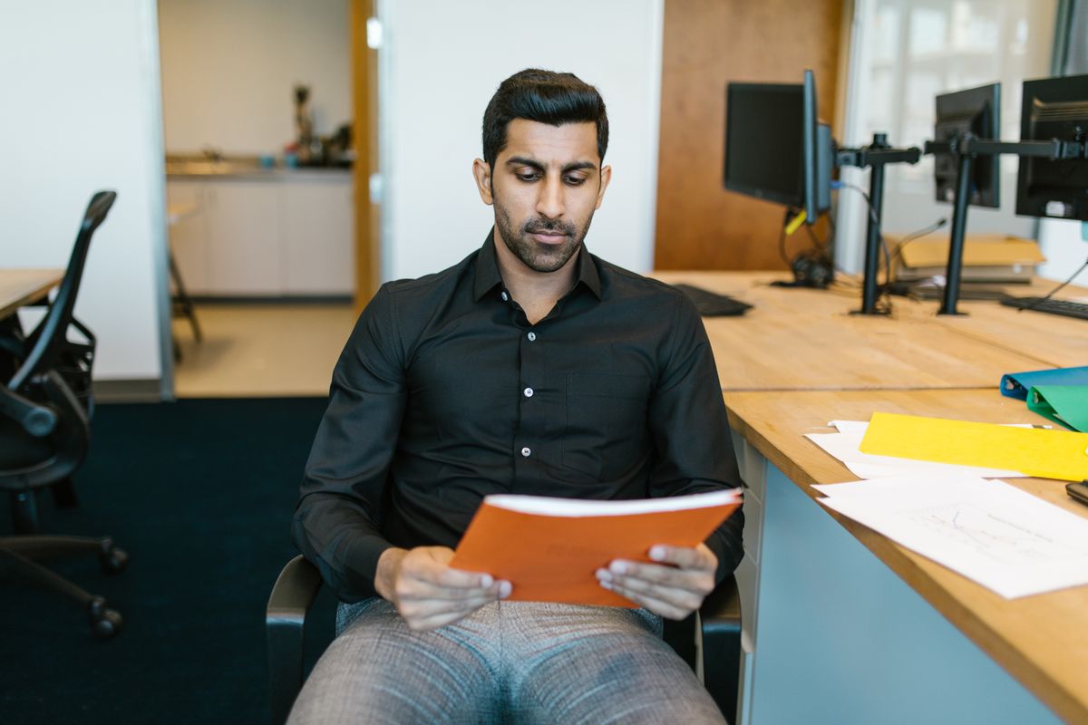 Indian professional reviewing a document while weighing a decision in an office