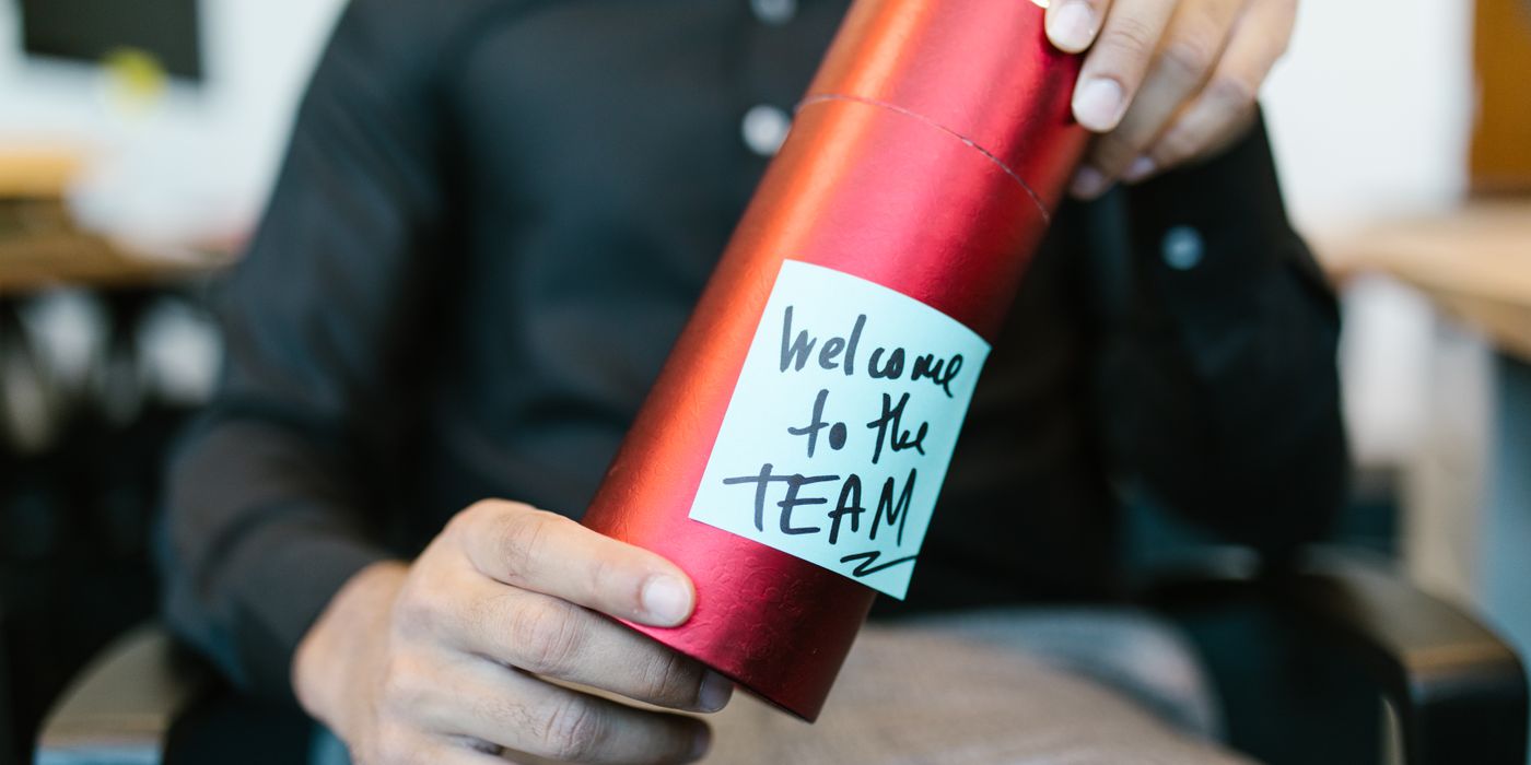 A red gift box held by a person with a welcome to the team note, ideal for new hire announcements.
