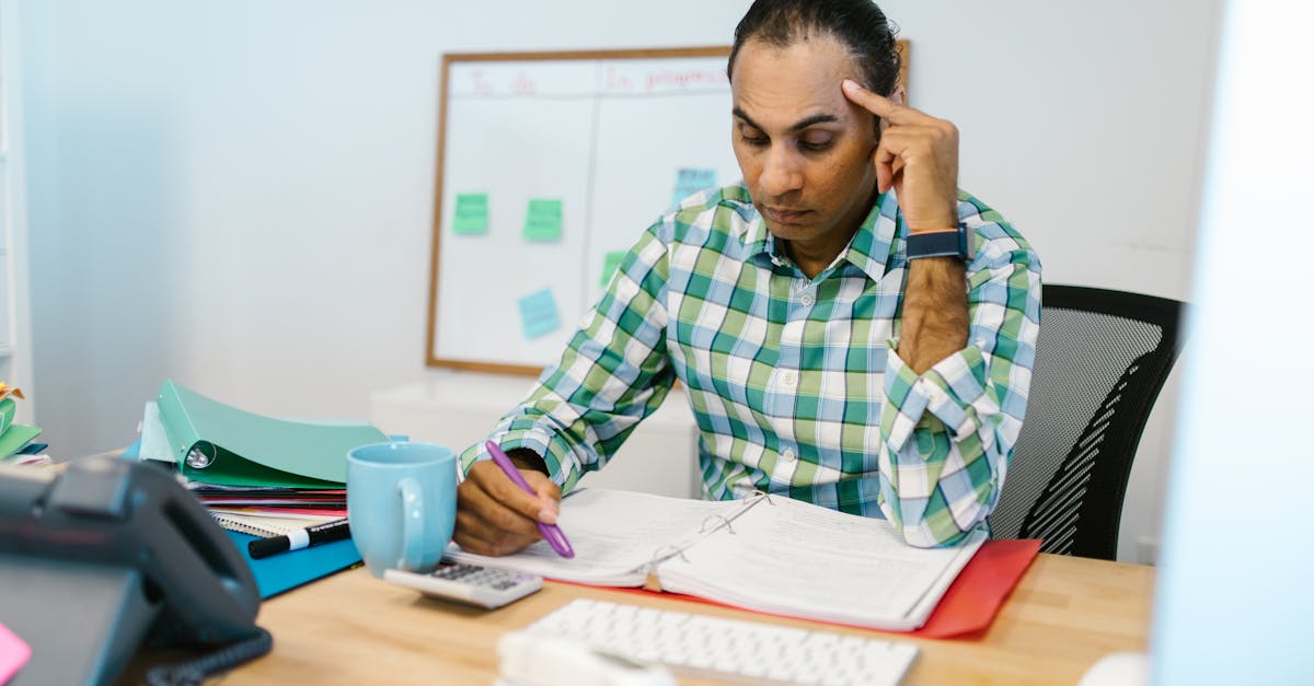 Person sitting alone at a desk with spreadsheets, looking stressed