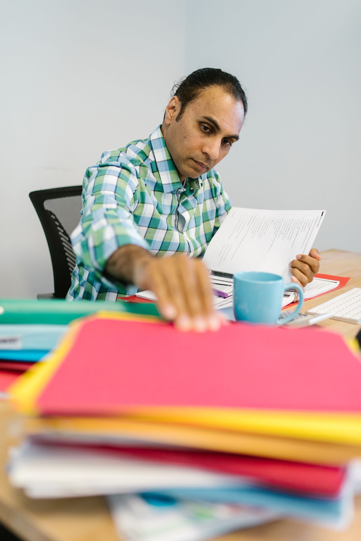 Indian professional sorting through colour-coded folders while comparing options at his desk