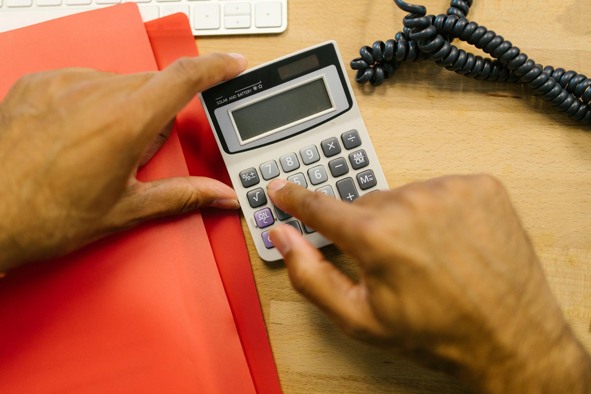 Close-up of hands using a calculator at a desk in an office setting.