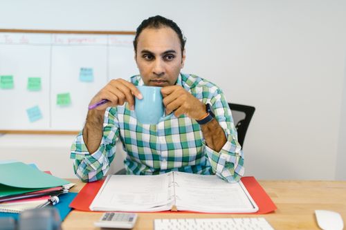 Free Focused office worker reviewing documents while sipping coffee from a mug. Stock Photo