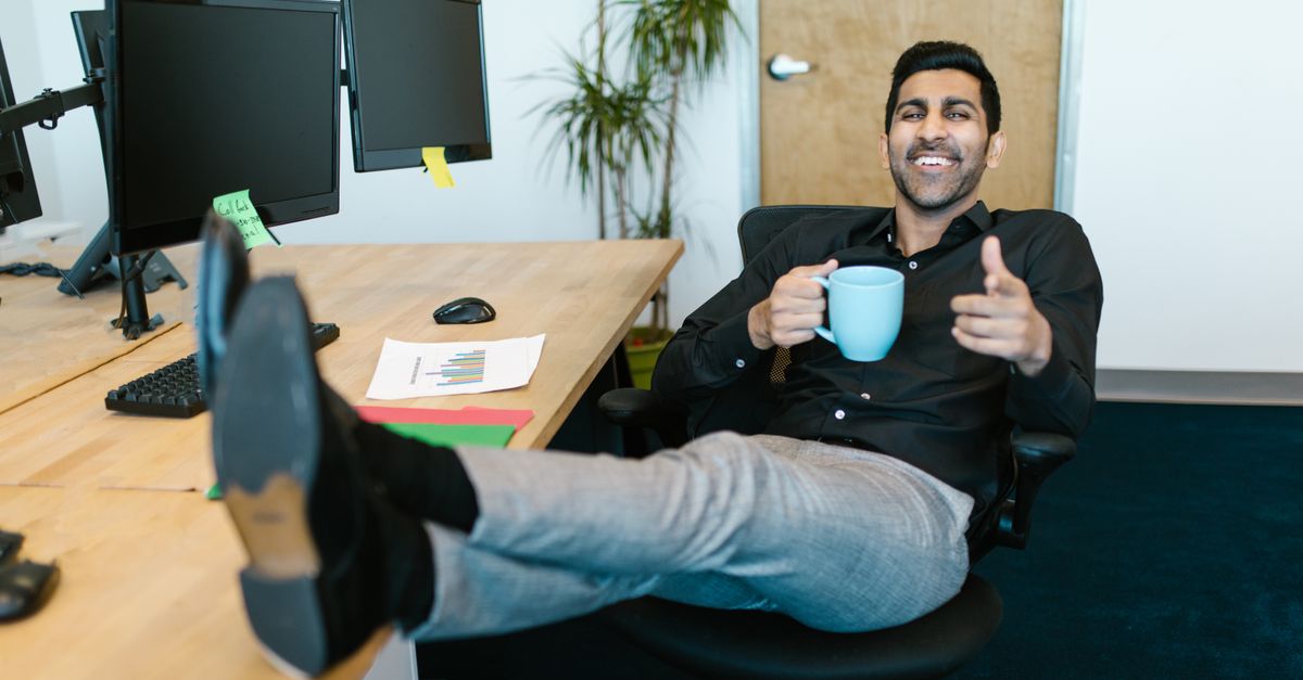 Smiling man relaxes in office with a mug, showing a casual work environment.