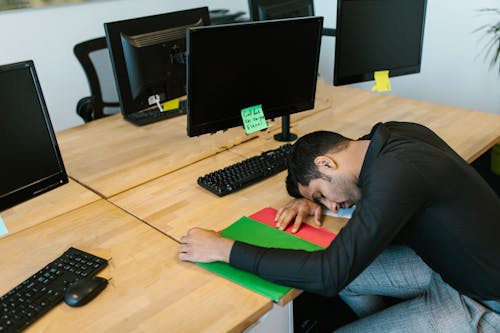 Man in Black Long Sleeve Shirt Sleeping in Front of a Computer