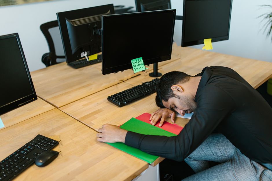 Trabajador de oficina exhausto que se queda dormido en el escritorio con monitores y teclado.