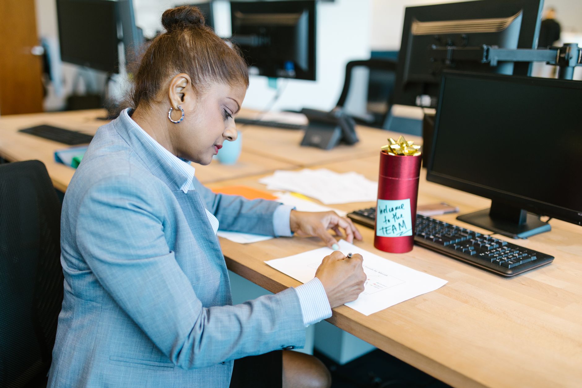 A focused woman working at her desk in a modern office setting with a welcome gift on display.