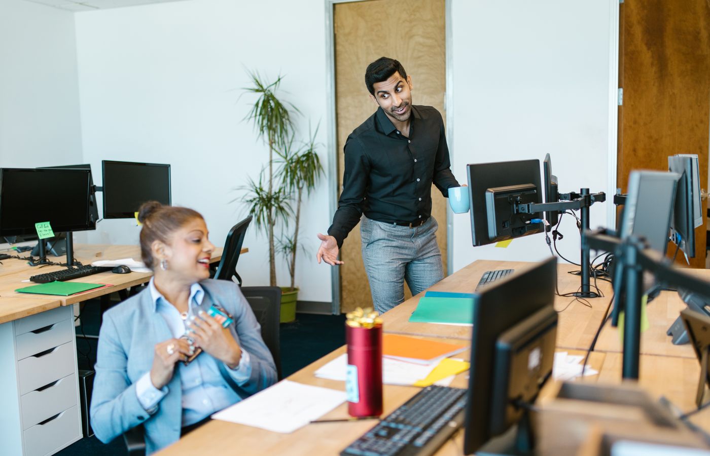 Two colleagues engaging in a cheerful conversation in a modern office setting.
