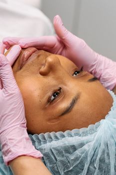 Close-up of a woman receiving a facial treatment in a medical clinic, wearing a bouffant cap.