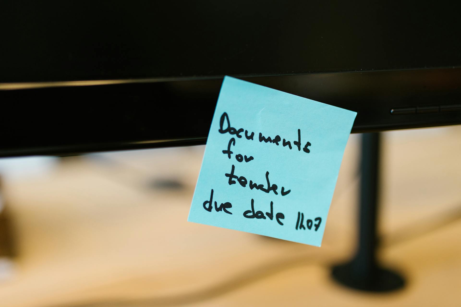 Close-up of a blue sticky note with a reminder attached to a computer monitor.