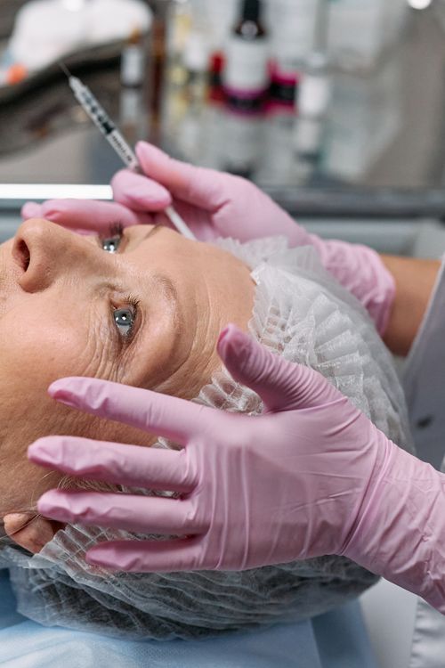 Free Close-up of a senior woman receiving a cosmetic injection in a clinical setting with gloves and a hairnet. Stock Photo