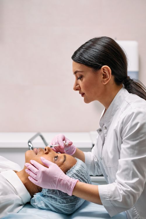 Free A female dermatologist applying a facial treatment to a patient in a medical clinic setting. Stock Photo