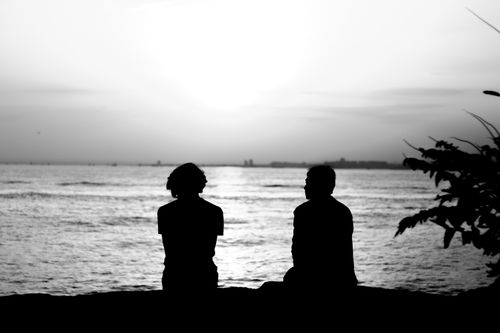 Free A silhouette of a couple sitting by the ocean, capturing a serene sunset view. Stock Photo