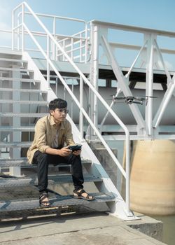 Man sitting on steps controlling a drone with a remote outdoors during daytime.