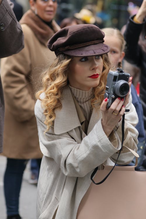 Fashionable Woman Standing among the Crowd and Holding a Film Camera 