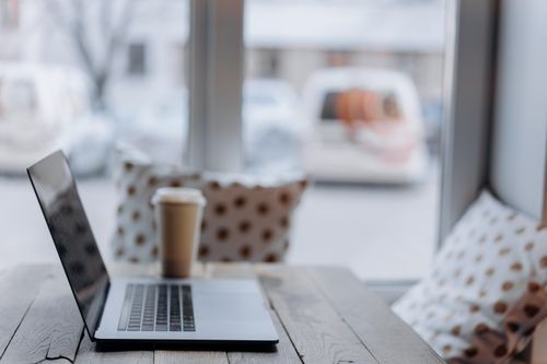 Free Cozy workspace with a laptop and coffee cup by a window, ideal for productivity. Stock Photo