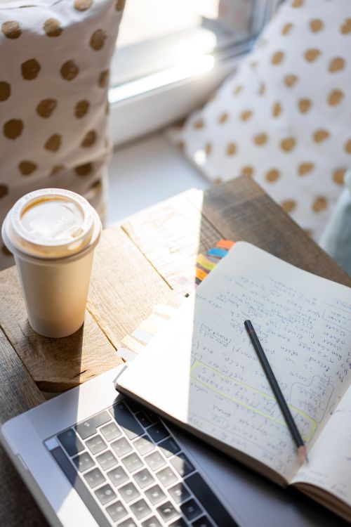 Free A cozy workspace setup featuring a coffee cup, open notebook, and laptop, perfect for productivity. Stock Photo
