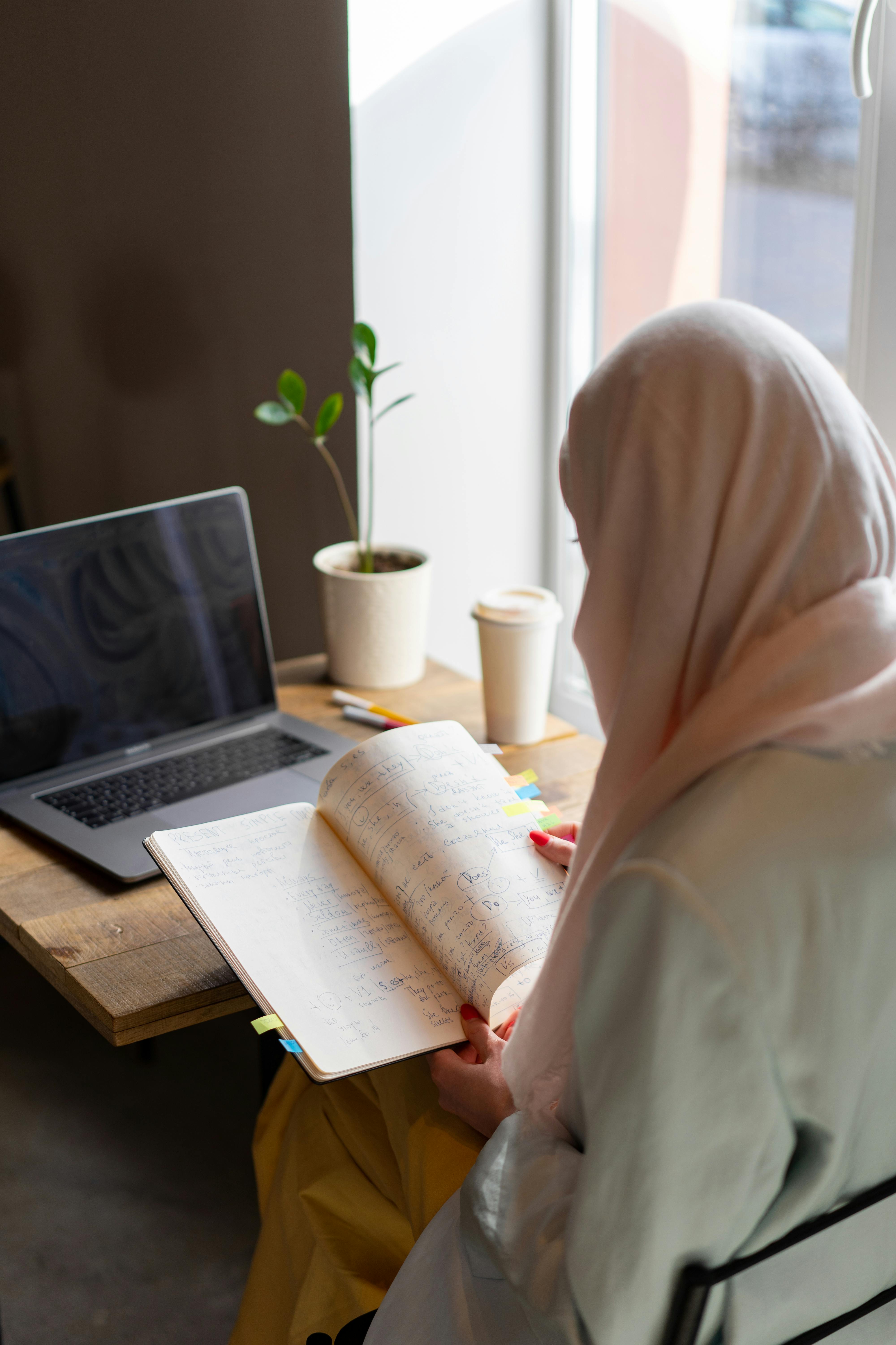 person in white hijab sitting in front of macbook pro on brown wooden table