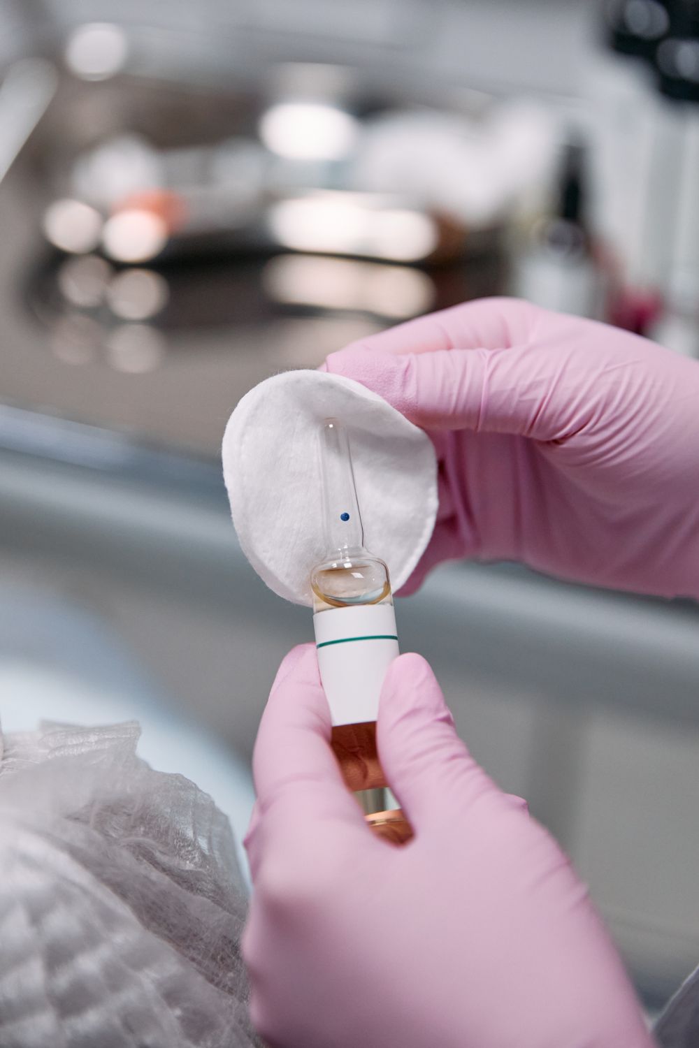 Gloved hands opening an ampoule for a skin treatment