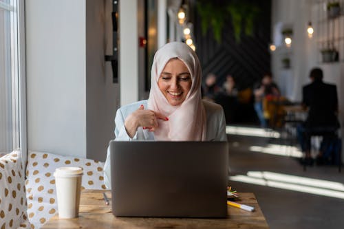 A Woman Wearing Hijab Smiling while Looking at Her Laptop