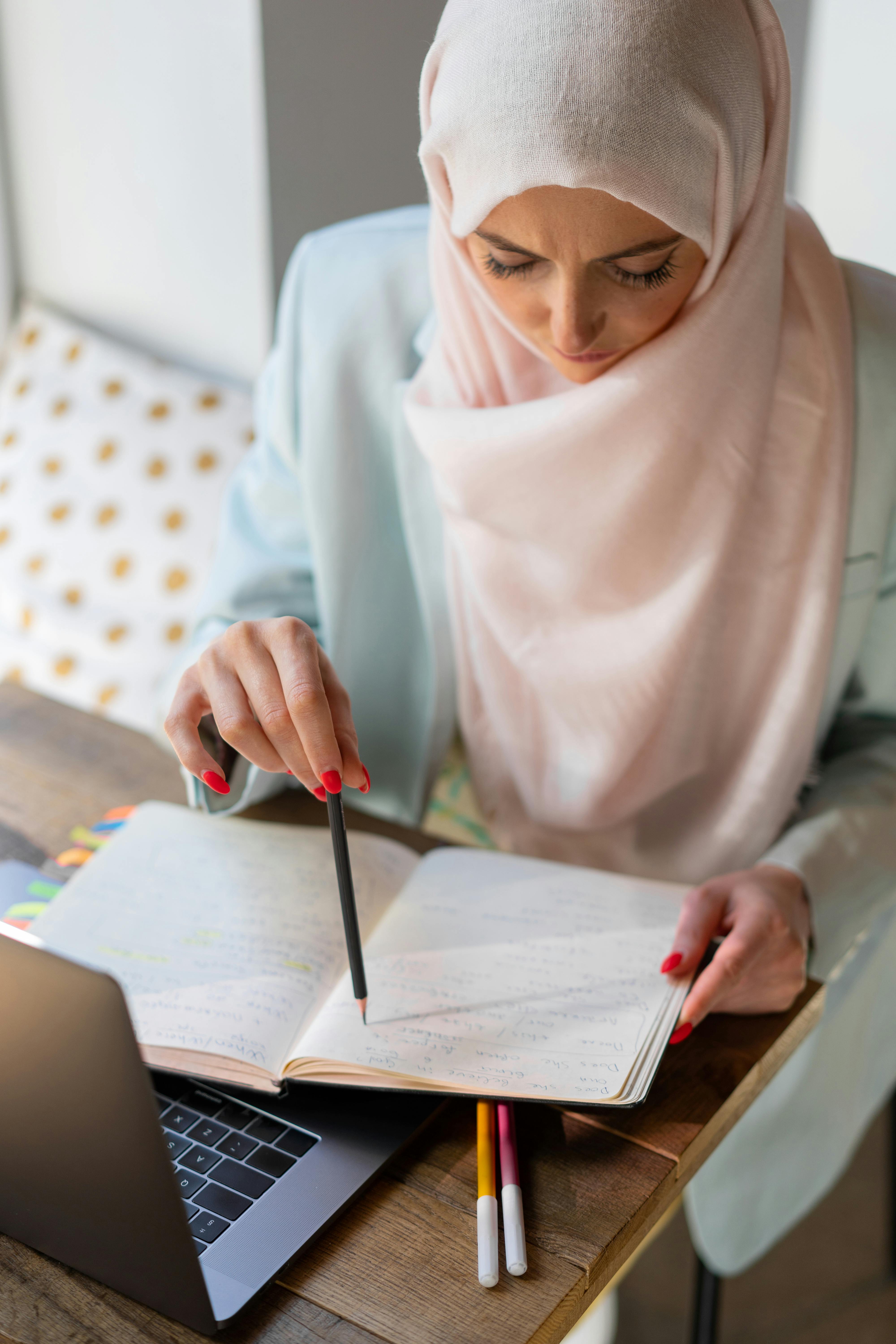 woman in white hijab holding pen writing on white paper