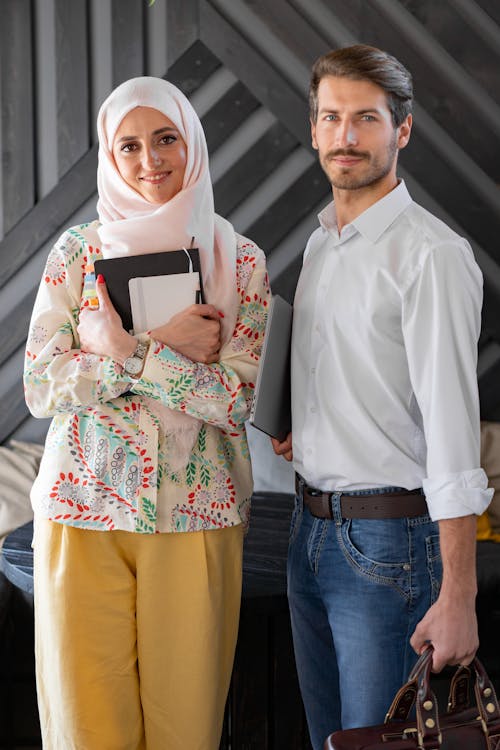 Free A Woman in Hijab Holding Notebooks Standing Beside a Man in White Long Sleeve Shirt Stock Photo