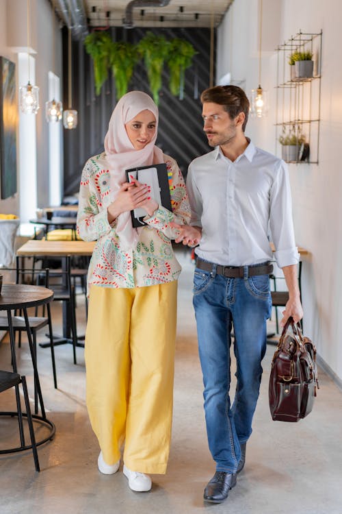 Free A Man in White Shirt Holding a Leather Bag Talking to a Woman Carrying a Notebook Stock Photo