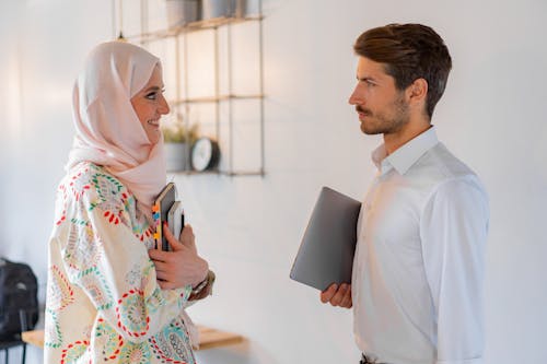 Free Woman Holding a Notebook Talking to a Man Holding a Laptop Stock Photo