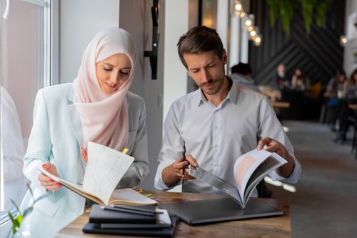Free A man and woman study together with books in a bright, modern cafe setting. Stock Photo