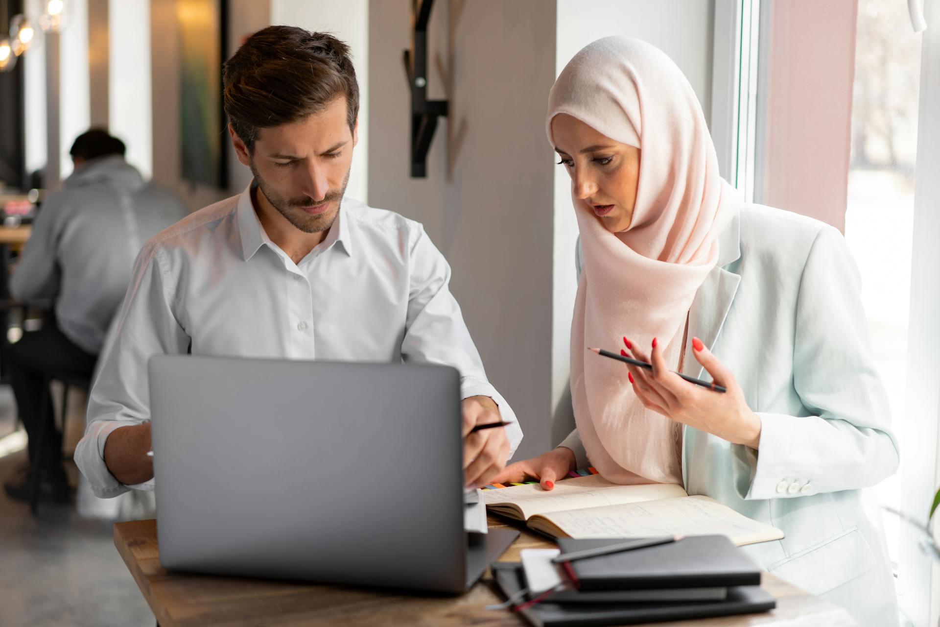 Two professionals in a modern office setting collaborating on a project using a laptop.