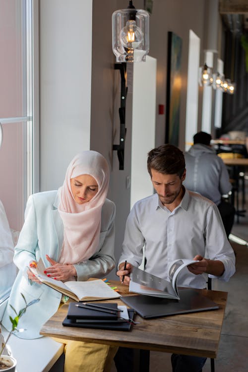 Free Woman Wearing Hijab Sitting Beside a Man Holding a Brochure Stock Photo