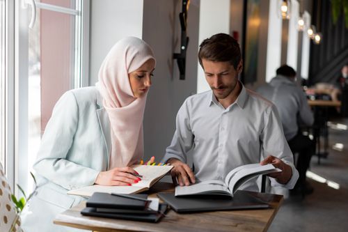 Free Two professionals in a modern setting collaborating and taking notes during a meeting. Stock Photo