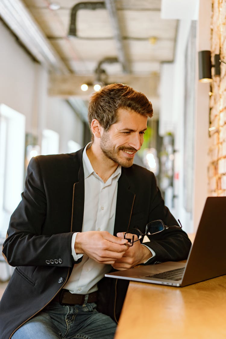 A Man In Black Suit Smiling While Looking At His Laptop