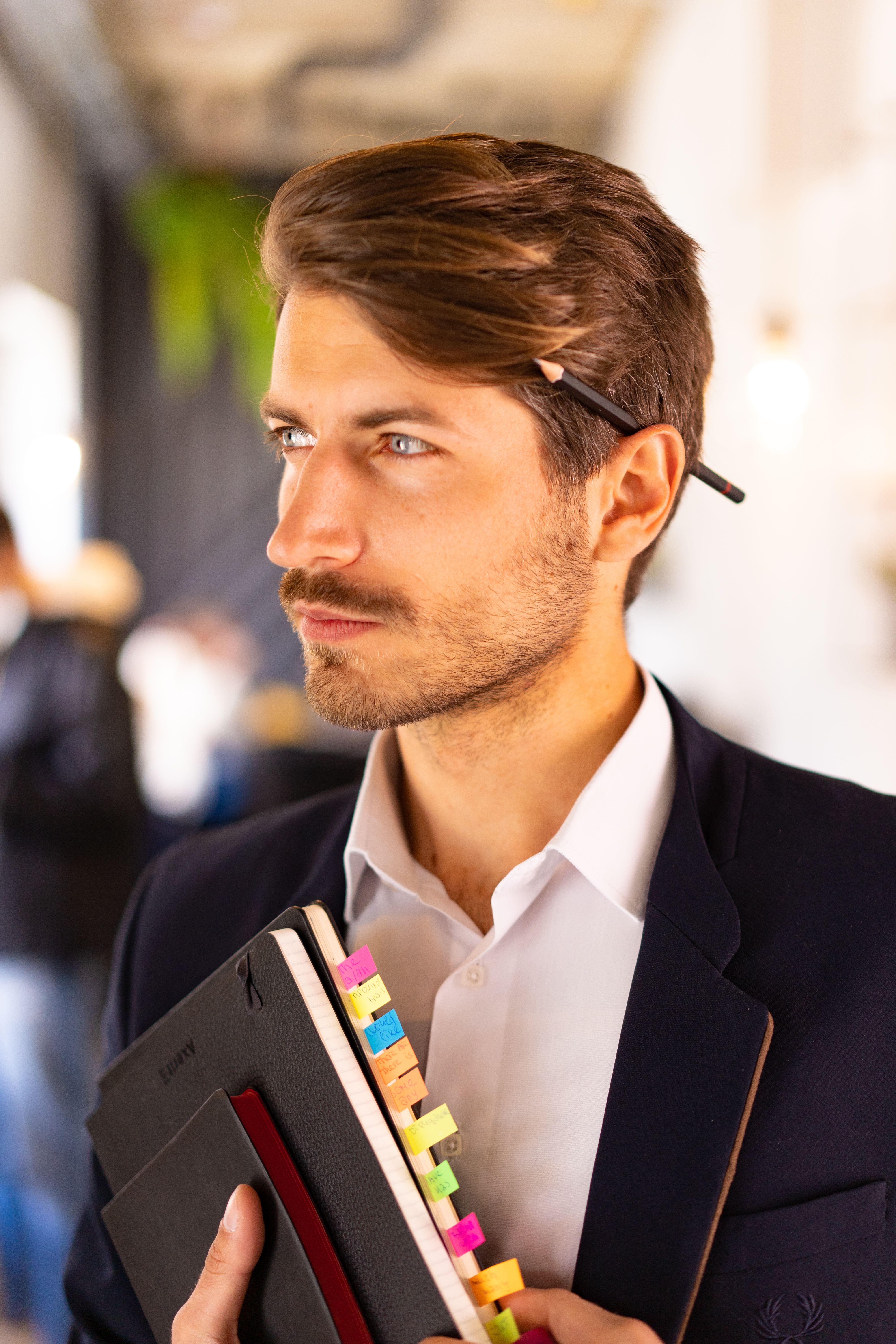 Business professional in a suit holding notebooks with colorful tabs in an indoor office environment.