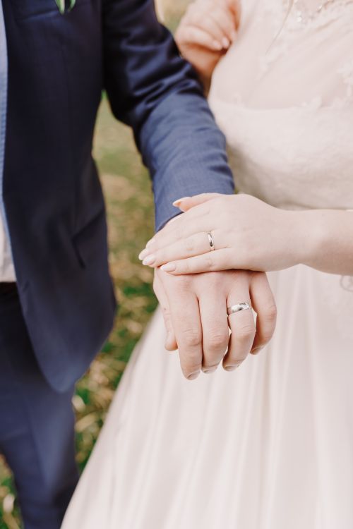 Free Close-up of bride and groom holding hands displaying wedding rings, symbolizing unity and love. Stock Photo
