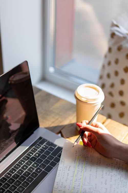 Free Sunlit workspace with a laptop, coffee cup, and notes, perfect for focused work or study. Stock Photo