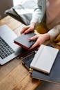 Woman's Hand Holding a Pen and Notebook Near a Laptop