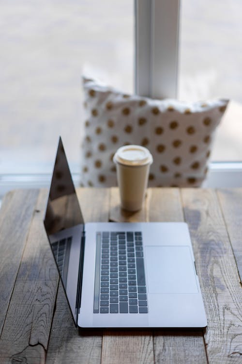 Free Silver Macbook on Wooden Table Beside a Paper Cup Stock Photo