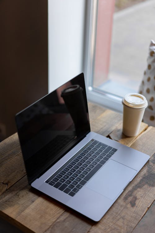 Free Silver Macbook on Wooden Table Beside a Paper Cup Stock Photo