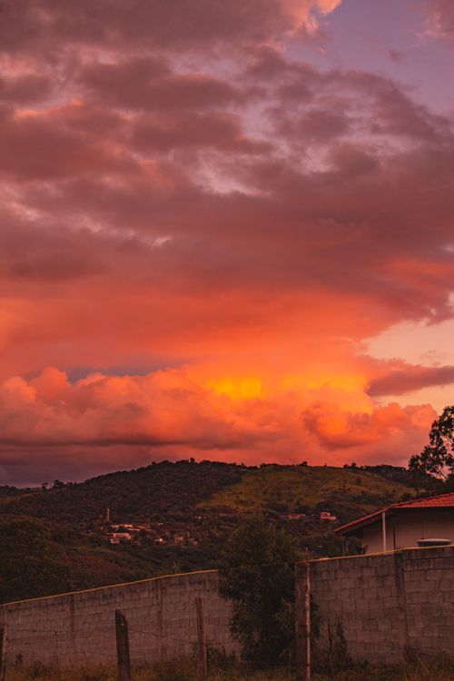 Free Stunning sunset with vibrant orange and pink clouds over rolling hills, visible above a concrete wall. Stock Photo