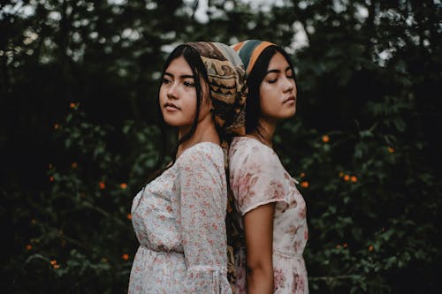 Twin Sisters Standing Back to Back Wearing Headscarves and Floral Dresses